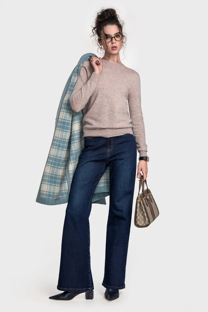 Rose-beige sweater with dark flared jeans and a blue plaid coat over the shoulder