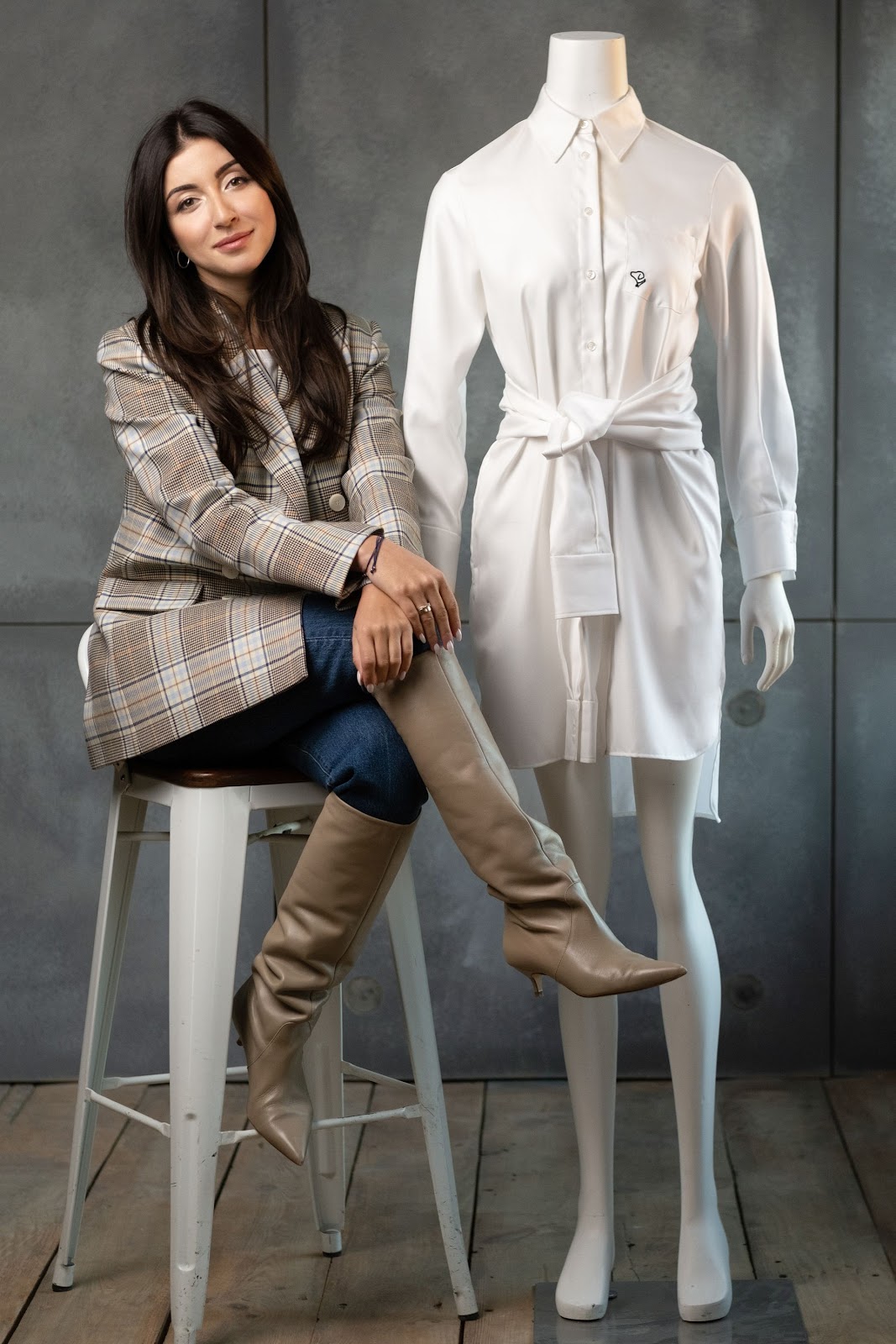 Viktorija, founder of Victorara, seated in the studio next to a mannequin wearing a white shirt dress
