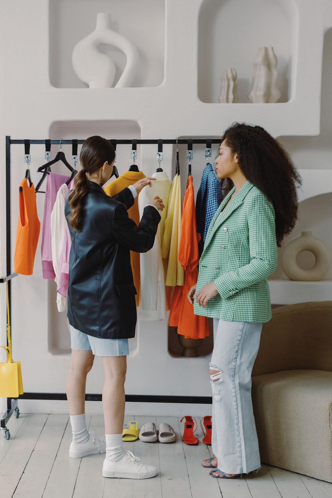 Two stylists selecting garments from a rail of colourful pieces in a bright studio