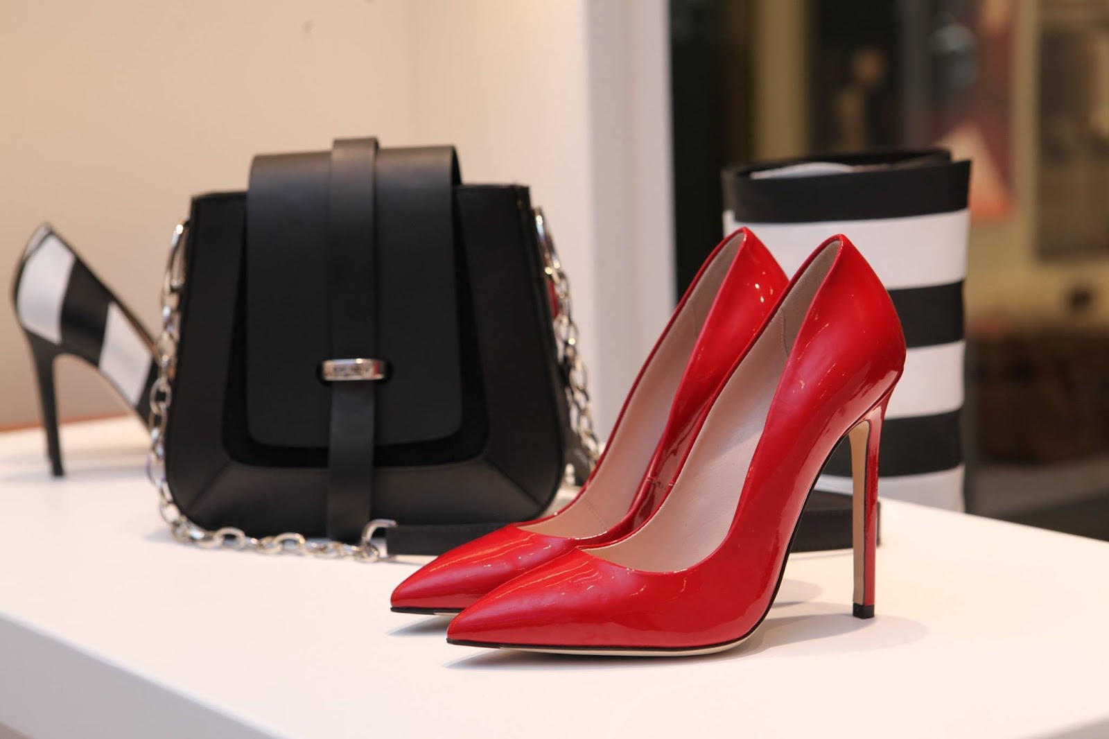 Red patent pumps beside a black leather bag and striped accessories on a display table